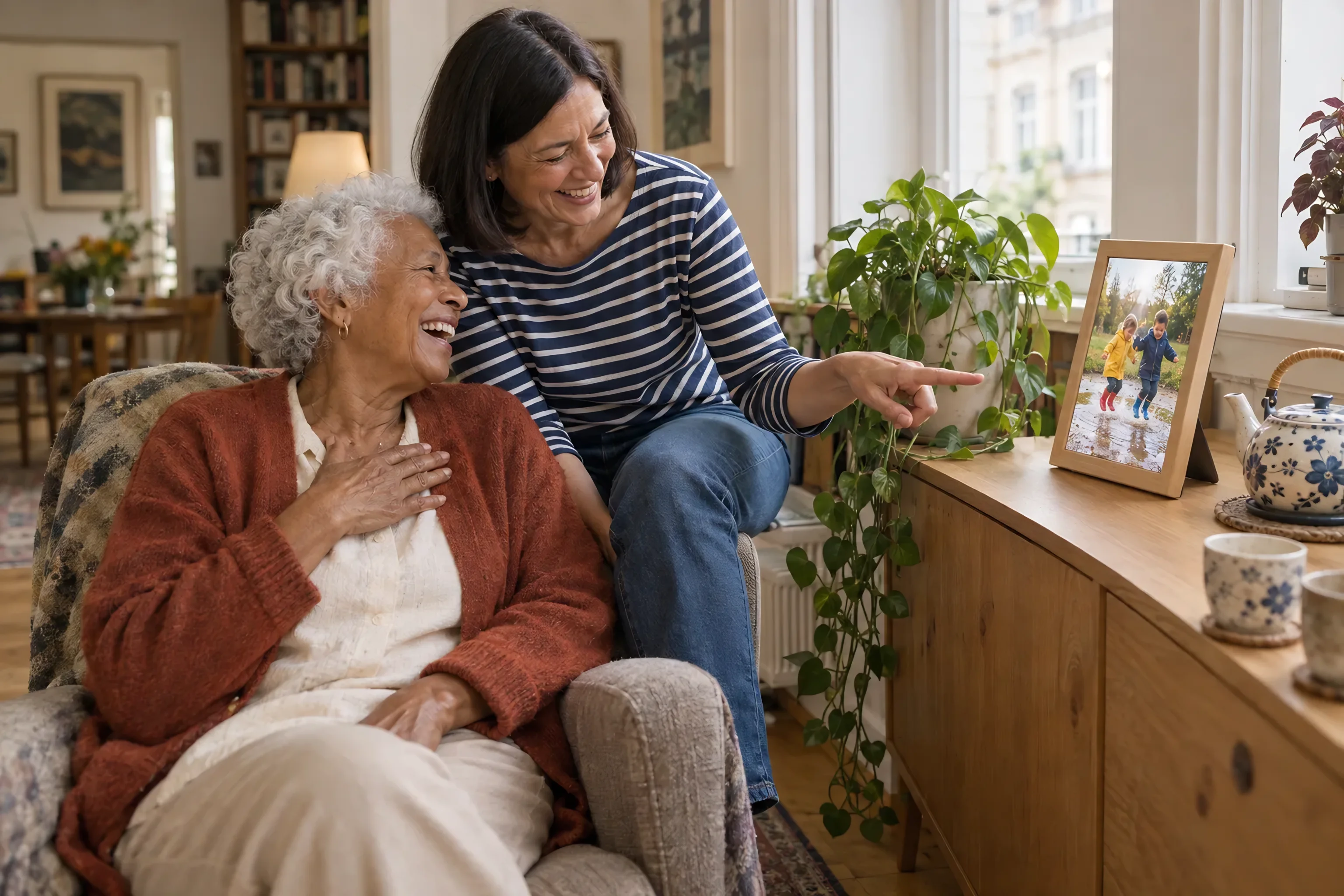 Ein digitaler Bilderrahmen in Holzoptik zeigt zwei Kinder in einer Pfütze; zwei Frauen lachen, eine zeigt auf den Rahmen.